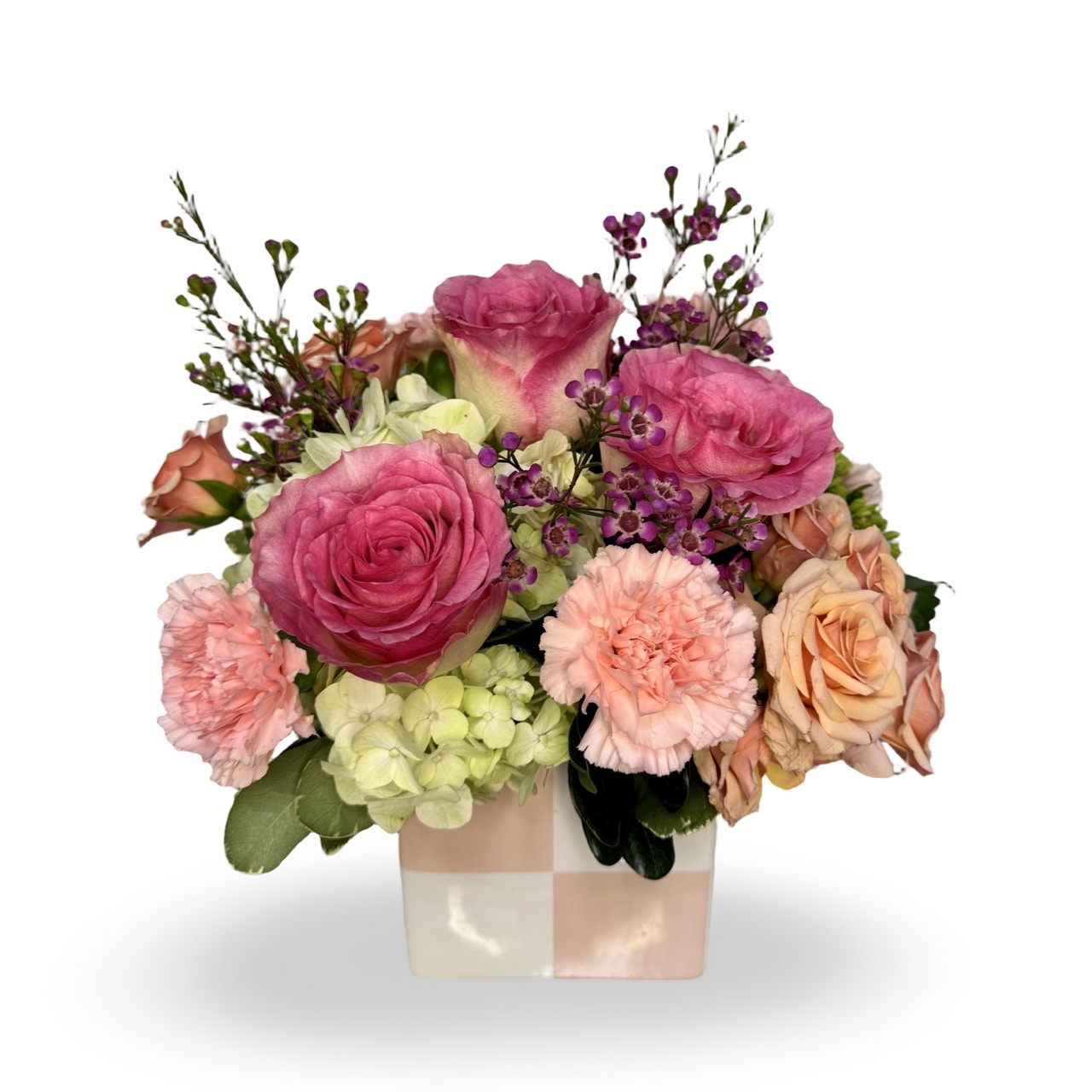 A pastel floral arrangement featuring pink roses, peach carnations, and hydrangeas in a checkered ceramic vase.