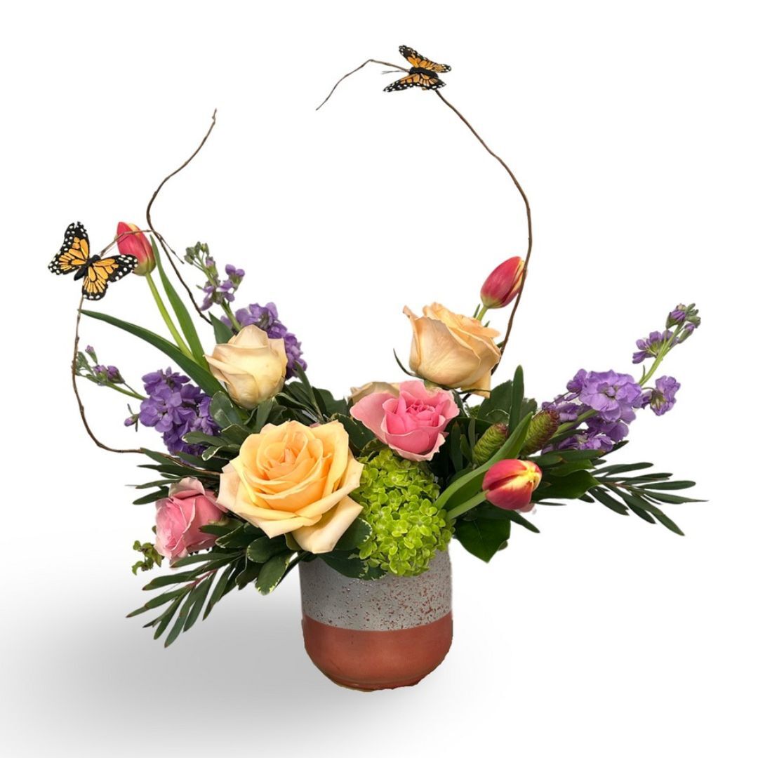 Elegant spring bouquet with pastel roses, purple flowers, and a butterfly, arranged in a ceramic pot.