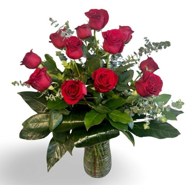Classic red rose arrangement with eucalyptus and glossy leaves in a ribbed glass vase.