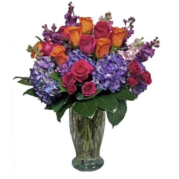 Colorful floral arrangement featuring roses and hydrangeas in shades of orange, pink, and purple in a tall vase.
