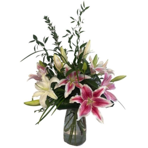 Fragrant lily arrangement with white and deep pink blooms, accented by lush greenery in a clear vase.