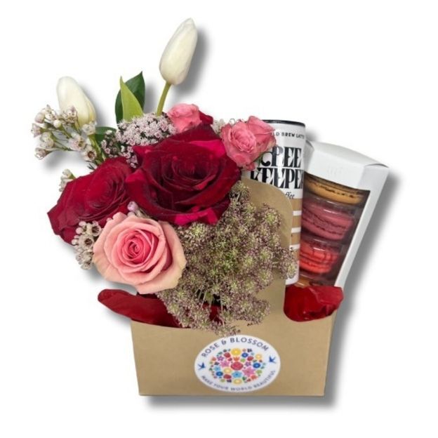 Floral gift set featuring roses, tulips, cold brew coffee, and a box of colorful macarons in a kraft carrier.