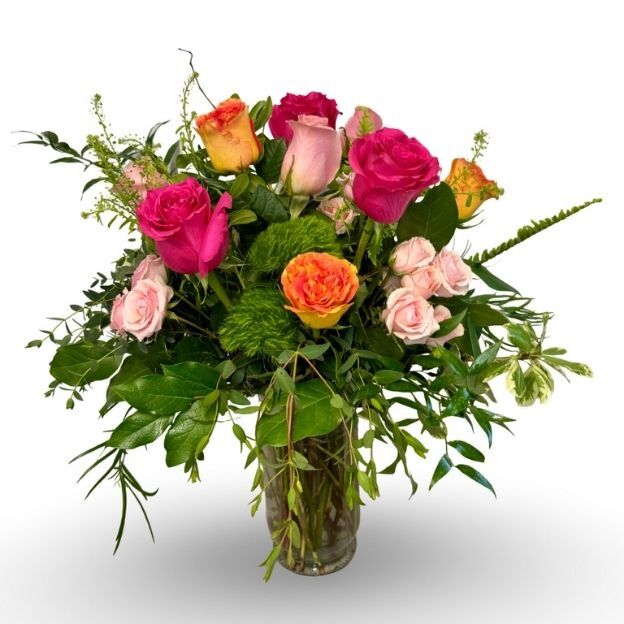 Bright bouquet with pink, orange, and yellow roses in a glass vase, surrounded by lush greenery.
