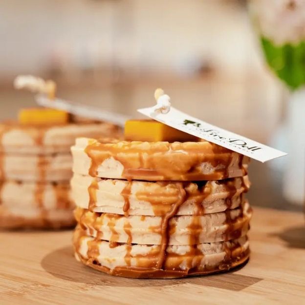 Decorative stacked candles with a caramel drizzle effect and a label tied with string, displayed on a wooden table.