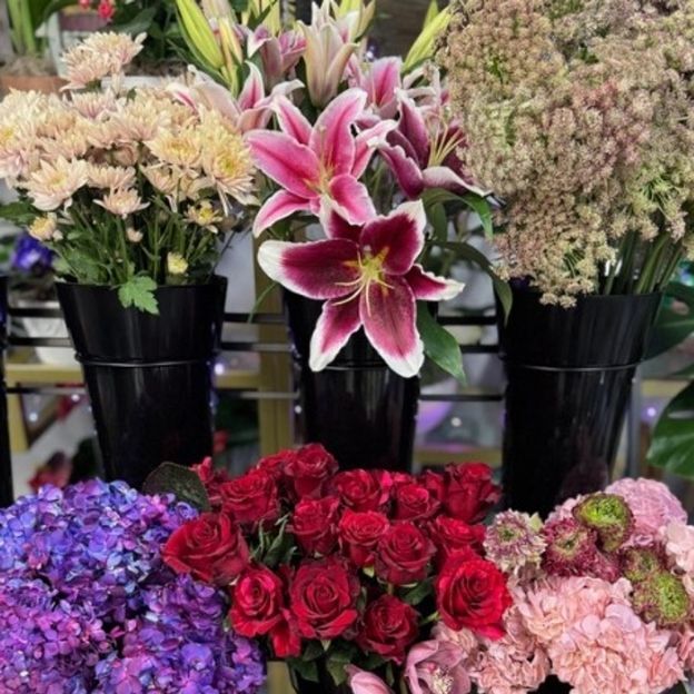 Assorted fresh flowers including lilies, roses, chrysanthemums, and hydrangeas arranged in black containers at a flower shop.