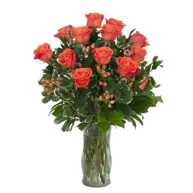 Bouquet of orange roses with lush green foliage and tiny pink berries arranged in a tall glass vase.