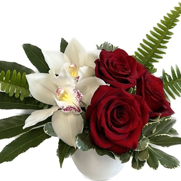 A floral arrangement with two white orchids, three red roses, and green ferns in a white vase.