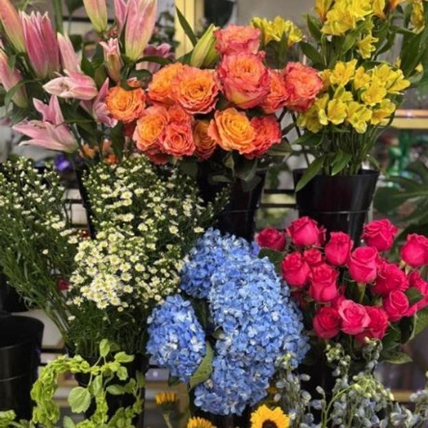 A colorful display of fresh flowers including pink lilies, orange roses, yellow blooms, blue hydrangeas, and red roses.