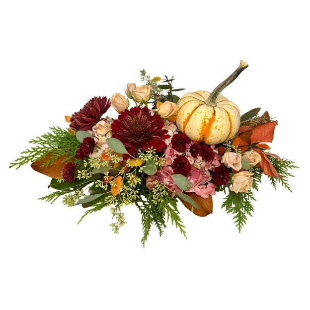 Autumn centerpiece featuring deep red flowers, soft roses, mixed greenery, and a decorative mini pumpkin.