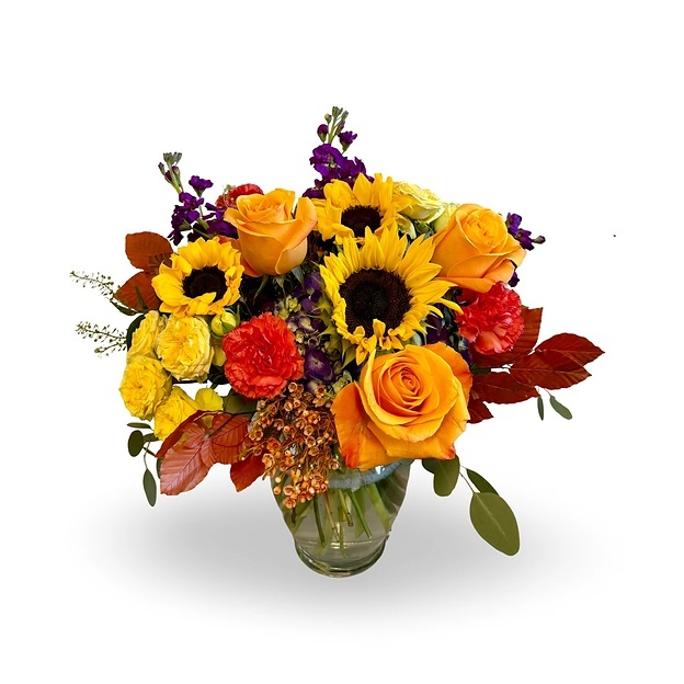 Sunflower bouquet with orange filler flowers and greenery in a glass vase.