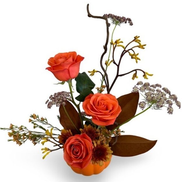 Minimal fall centerpiece featuring orange roses, twiggy branches, seeded fillers, and magnolia leaves in a mini pumpkin container.